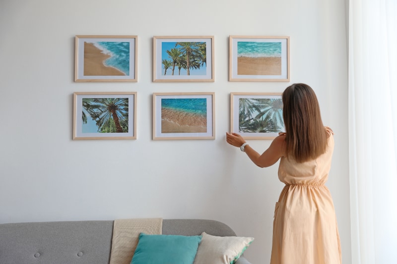 woman hanging up tropical photos on wall in staged home