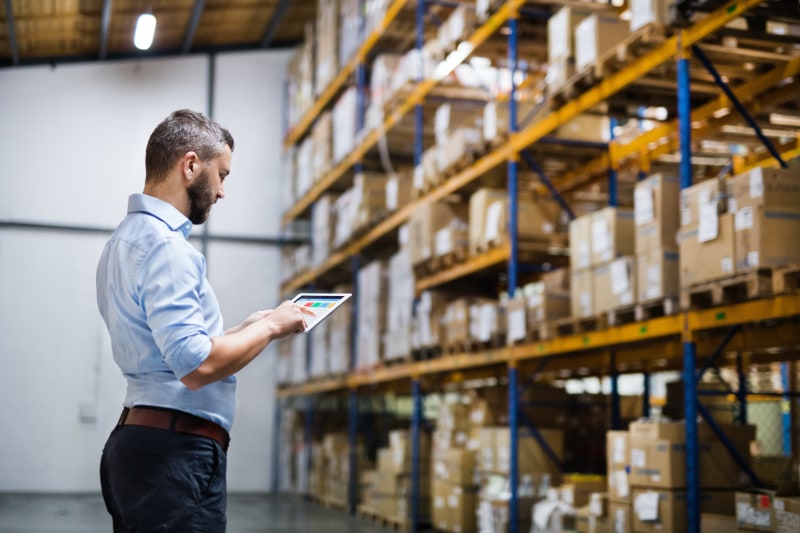 warehouse worker looking at tablet in front of tall shelves of boxes