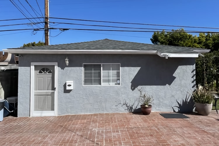 exterior of 3010 Dow; small gray stucco house with brick patio front