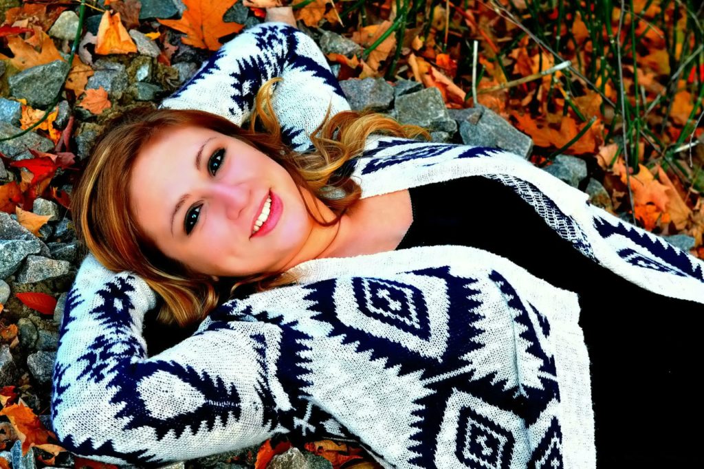 smiling young woman laying in rocks and fall foliage