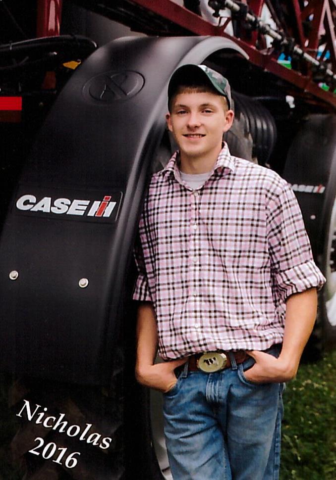 smiling young man leaning against large farm harvester equipment