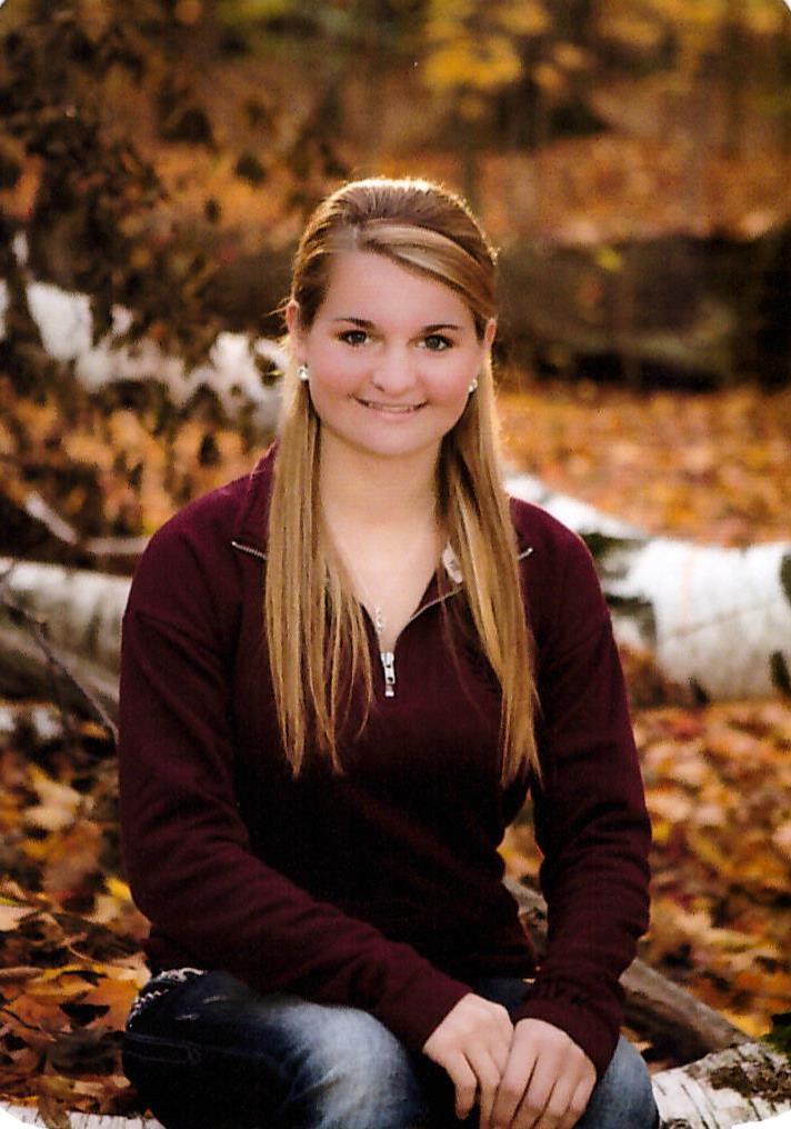 smiling young woman sitting on a birch log in fall foliage