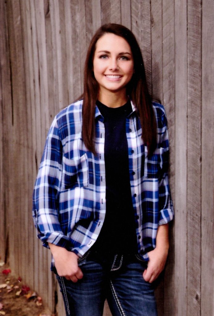smiling young woman in blue flannel leaning up against wooden wall