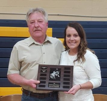 smiling young woman and older man holding plaque in a high school gym