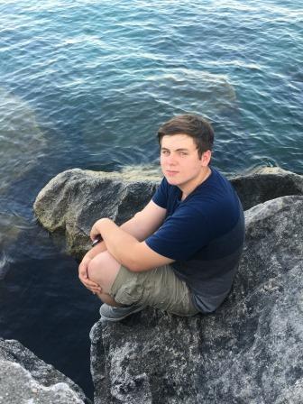 young man posing on large rocks near lake