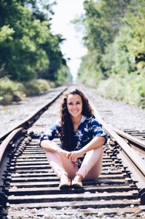 smiling young woman sitting on railroad tracks