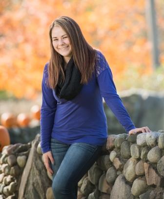 smiling young woman leaning on short rock wall/fence