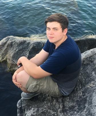young man posing on large rocks near lake