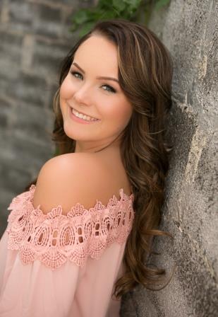 smiling young woman with pink off the shoulder top leaning up against stone wall
