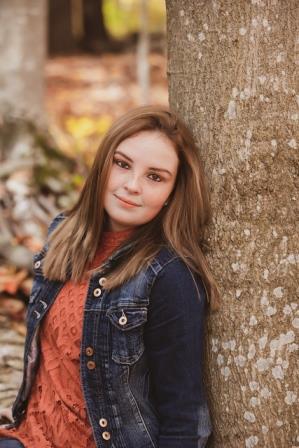 young woman in jean jacket leaning up against a tree trunk