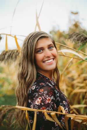 smiling young woman in floral shirt surrounded by ornamental grasses