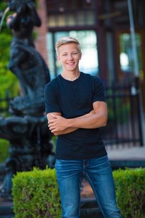 smiling young man with arms crossed posing in front of a fountain