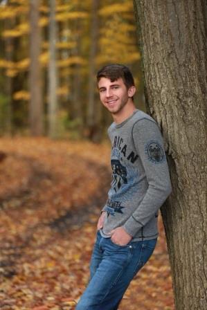 smiling young man leaning up against a tree trunk