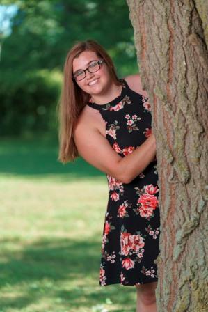 smiling young woman peeking around a large tree trunk