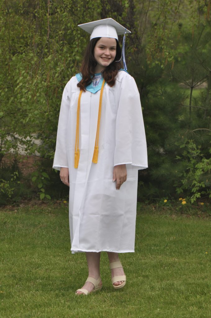 smiling young woman in white cap and gown posing on a lawn
