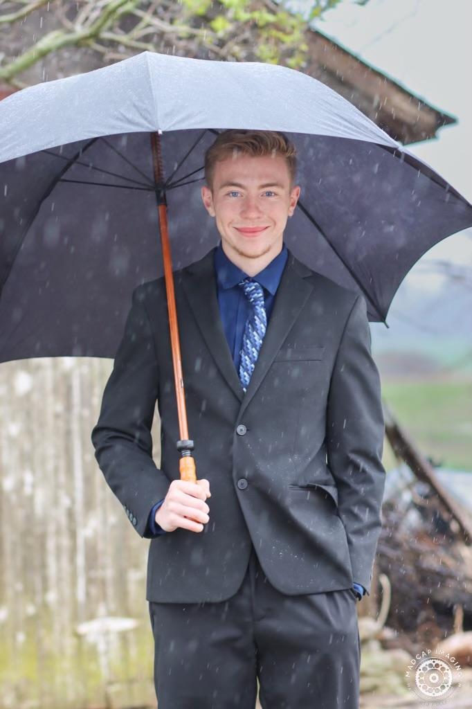 smiling young man in a suit with a large umbrella on a rainy day
