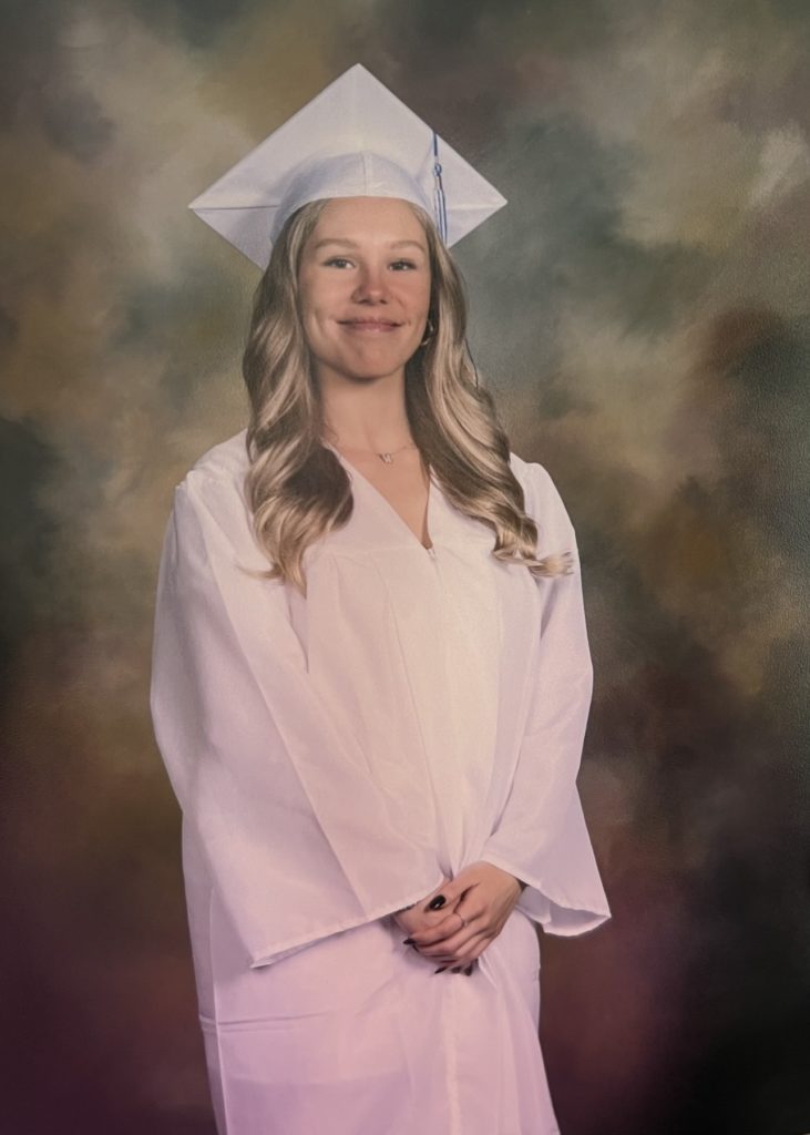 young woman with long blonde hair in white graduation camp and gown