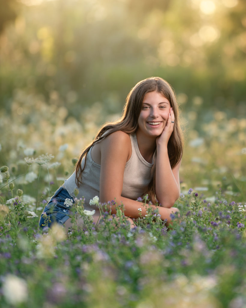 young woman in tank top and jean shorts kneeling in a field of wildflowers